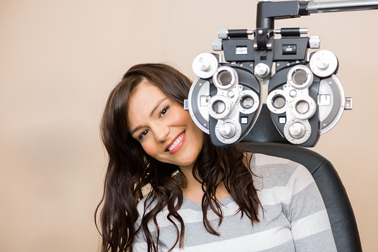 Portrait of happy young woman sitting behind phoropter during eye exam